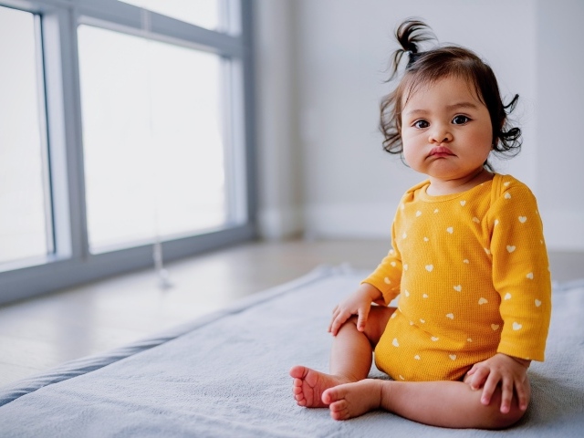 Маленькая смешная девочка сидит у окна