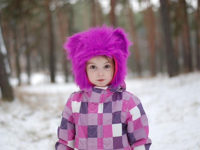 Маленькая девочка в меховой шапке в лесу зимой