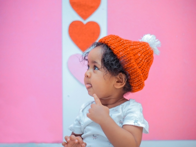 Маленькая девочка в вязаной шапке на розовом фоне