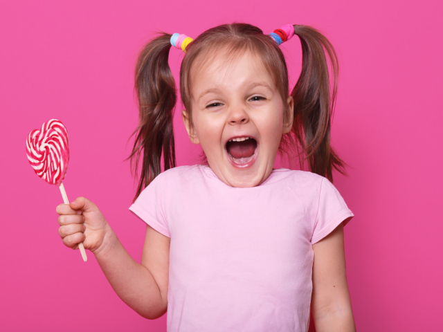 Маленькая девочка с леденцом на розовом фоне