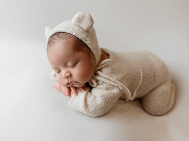 Маленький спящий ребенок в вязаном костюме на сером фоне
