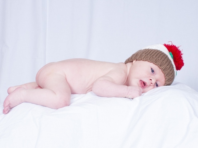 Новорожденный малыш в шапке на белой подушке