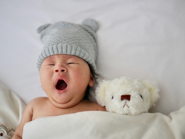 Новорожденный ребенок с игрушкой зевает в кровати