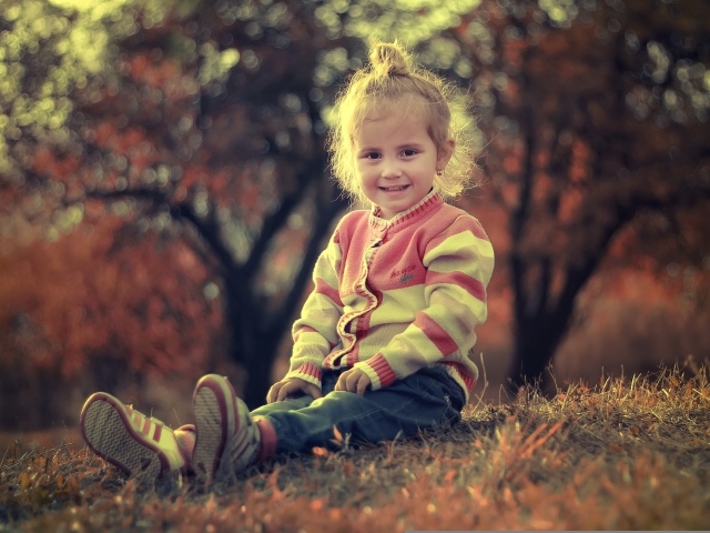 Настоящая маленькая девочка сидит на земле в лучах солнца