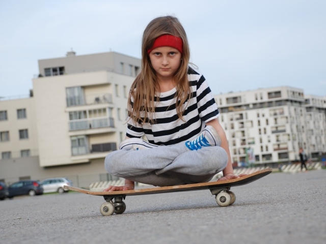 Серьезная девочка сидит на  скейтборде