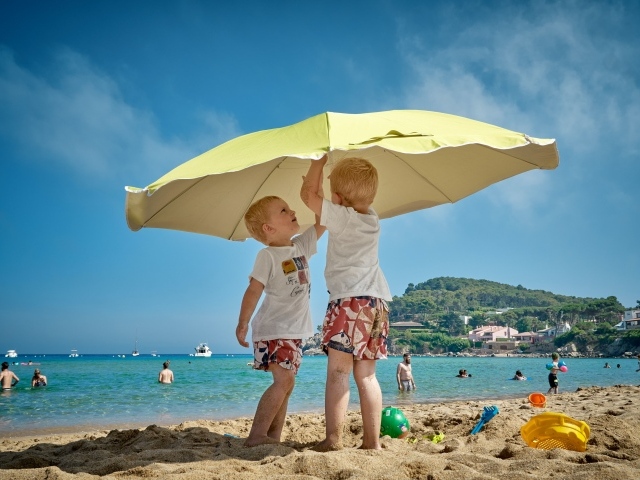 Два мальчика на пляже под зонтом