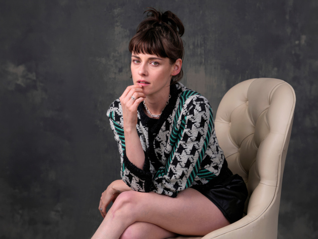 Актриса Кристен Стюарт сидит в кресле на фоне серой стены