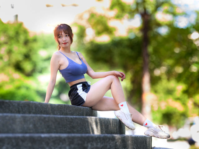 Спортивная азиатка в кроссовках сидит на ступеньках