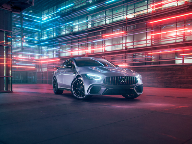 Серебристый автомобиль Mercedes AMG GT4 на фоне здания
