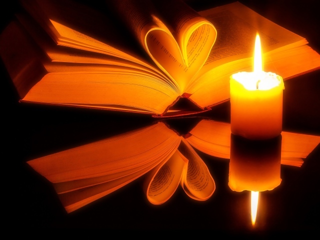 Открытая книга с зажженной свечой отражаются в черной поверхности