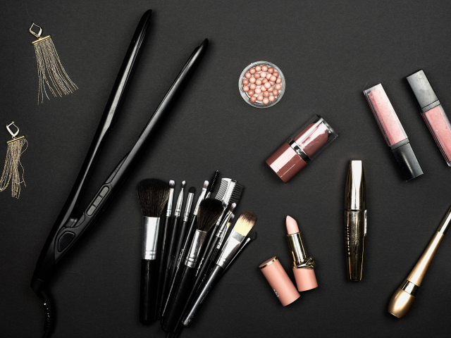 Кисточки с косметикой и плойкой на черном фоне