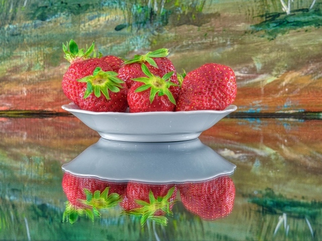 Белая тарелка с клубникой отражается в поверхности стола