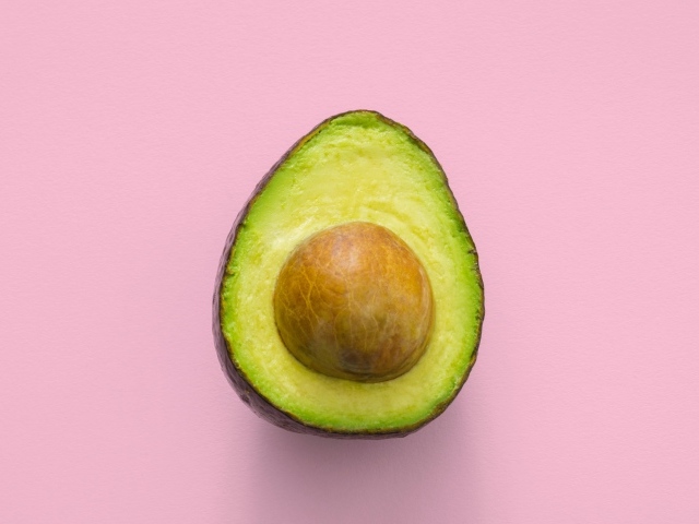 Половина авокадо с большой косточкой на розовом фоне