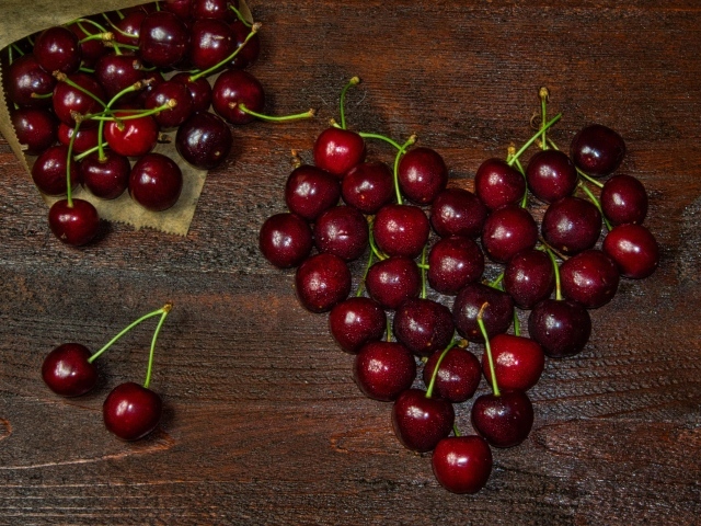 Сердце из спелых ягод черешни на деревянном столе