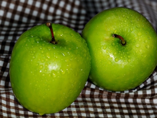Два мокрых зеленых яблока на скатерти