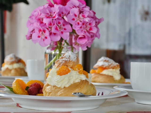 Булочки с кремом и фруктами на столе с букетом