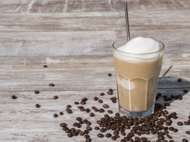 Кофе с мороженым в стакане на столе с кофейными зернами