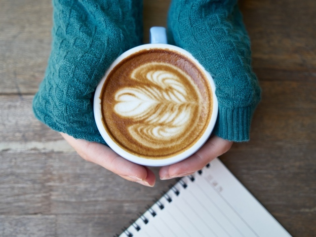 Горячая чашка кофе на столе в руках девушки