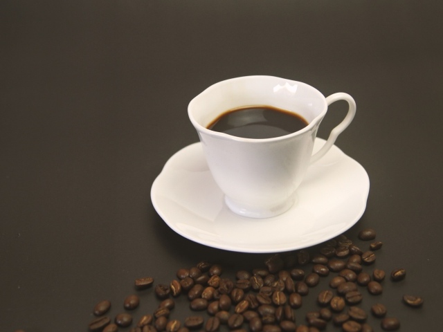 Белая чашка с кофе на столе с зернами