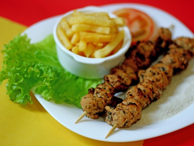 Шашлык на шпажках на столе с картофелем фри и листьями салата