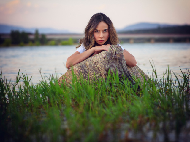 Девушка у воды прячется за камнем