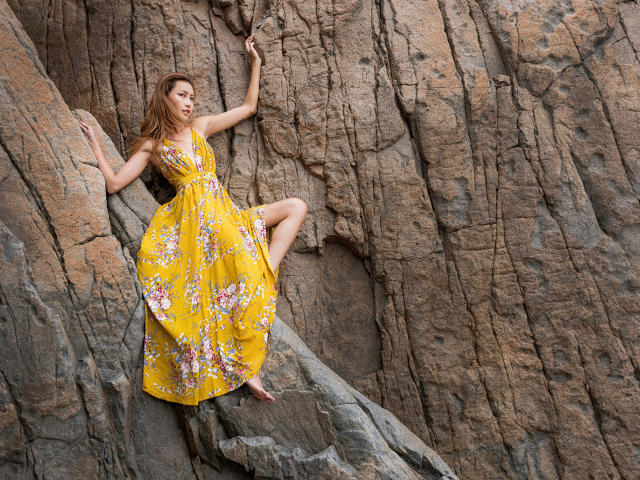 Девушка азиатка в красивом длинном платье позирует на скале