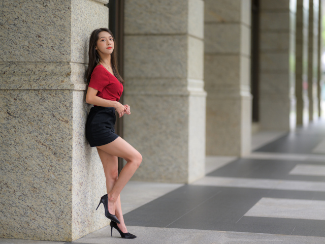 Азиатка в короткой черной юбке стоит у стены