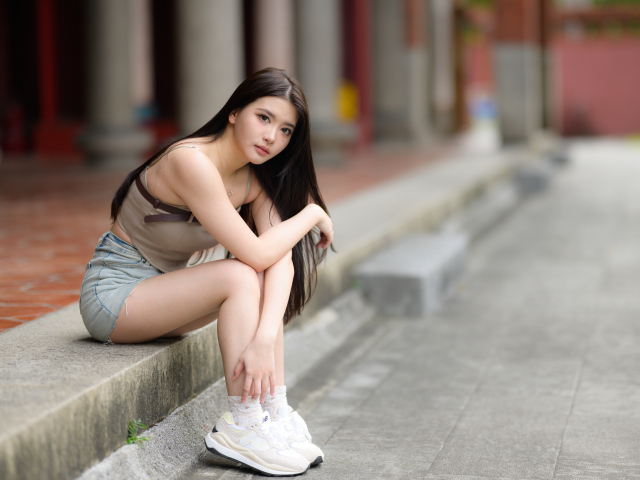Азиатка в белых кроссовках сидит на бордюре