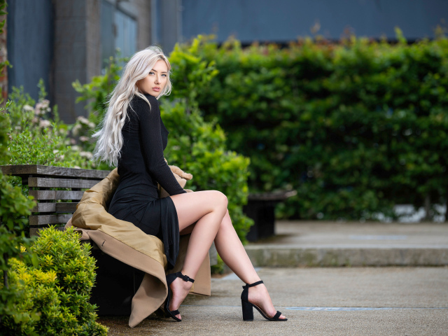 Красивая девушка в черном платье сидит на лавке