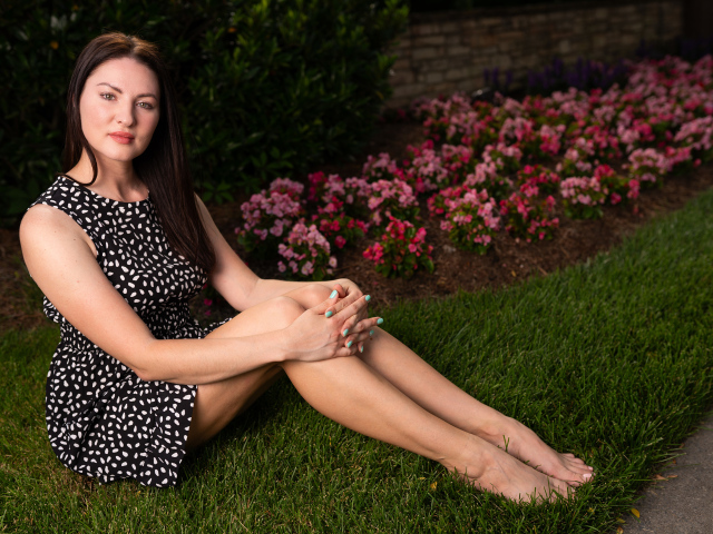 Красивая девушка в платье сидит у клумбы с цветами