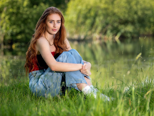 Красивая рыжеволосая девушка сидит в зеленой траве
