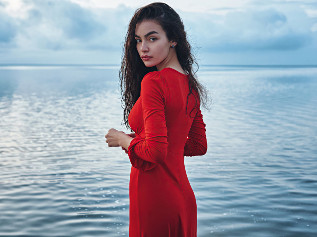 Милая девушка в красном платье стоит у воды