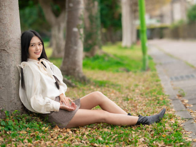 Улыбающаяся азиатка сидит под деревом в парке