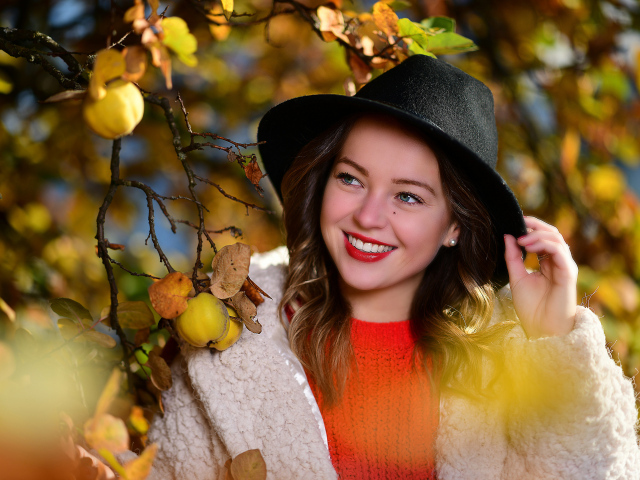 Улыбающаяся девушка в черной шляпе у дерева с яблоками