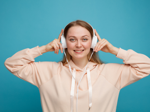 Улыбающаяся девушка в наушниках на голубом фоне