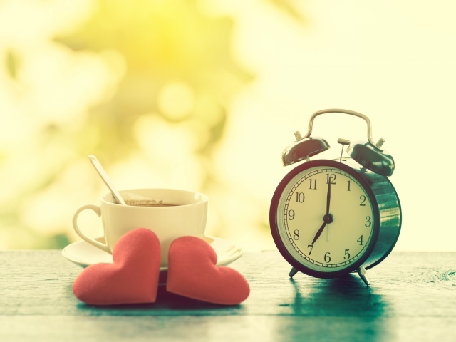 Будильник на столе с чашкой кофе и сердечками