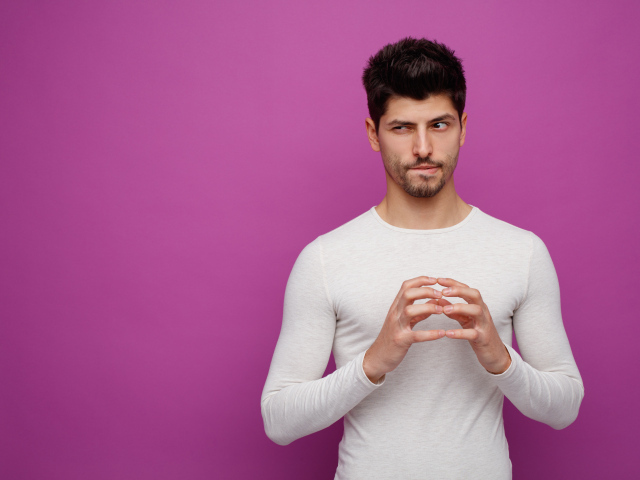 Хитрый мужчина в белом свитере на сиреневом фоне