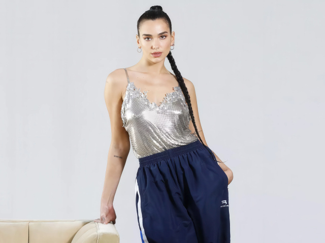 Певица Дуа Липа в спортивных штанах на сером фоне