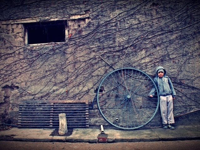 Мальчик с большим колесом стоит у стены