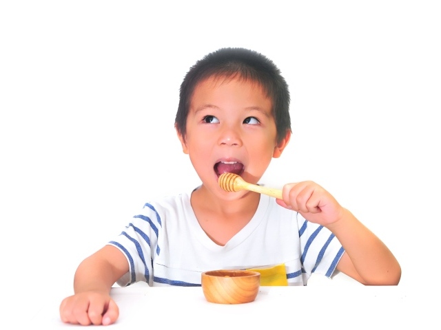 Мальчик азиат ест мед на сером фоне