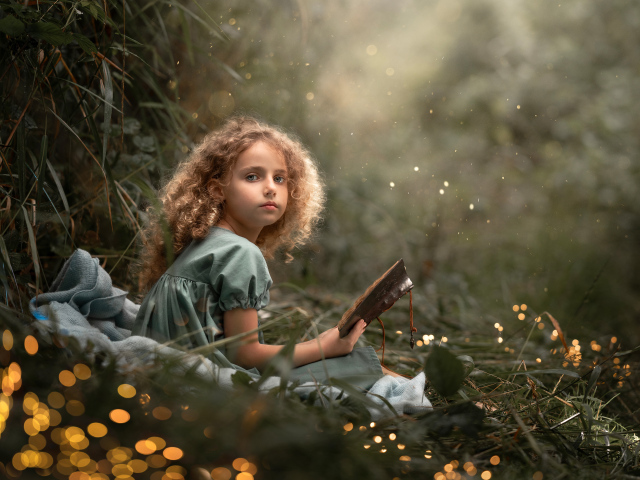 Милая девочка читает книгу сидя на траве