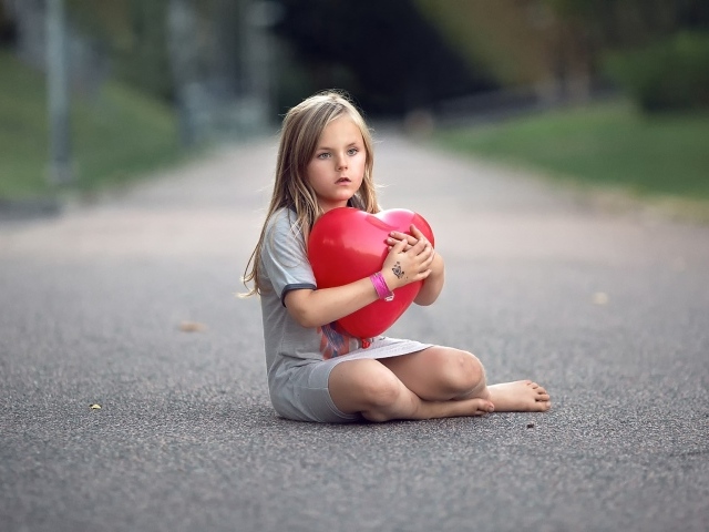 Девочка сидит на дороге с шариком в форме сердца