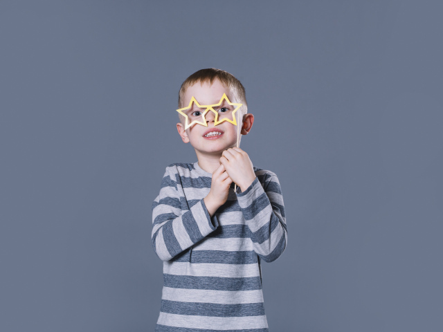 Маленький мальчик с очками в форме звезд на сером фоне
