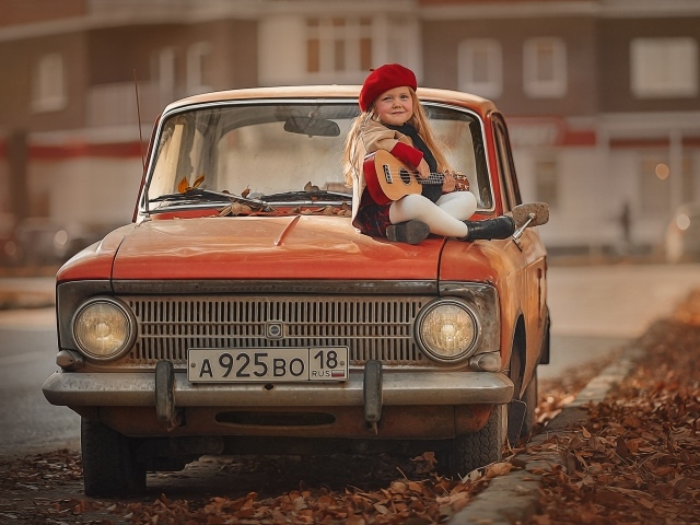 Маленькая девочка с гитарой сидит на красном автомобиле осенью