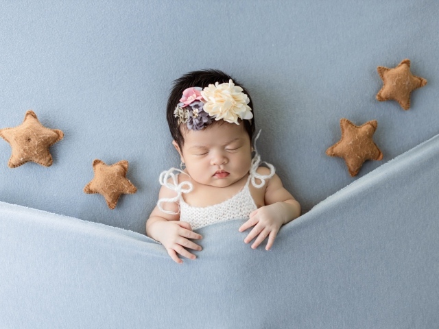 Новорожденная девочка с игрушечными звездами под серым покрывалом