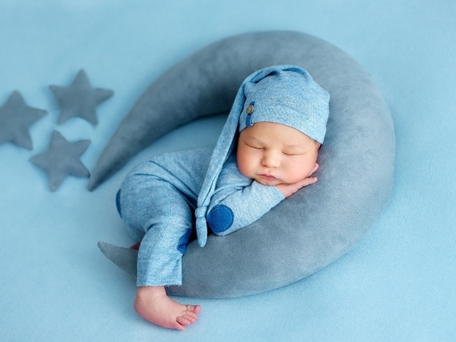 Новорожденный малыш спит на игрушечном полумесяце на голубом фоне