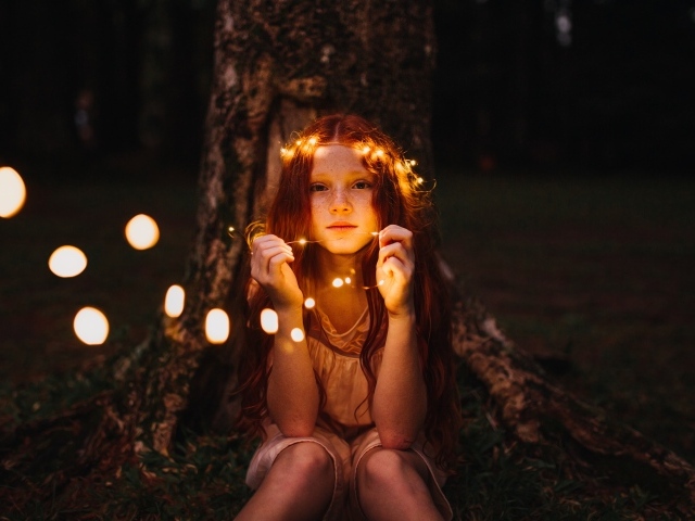 Рыжеволосая девочка с гирляндой под деревом