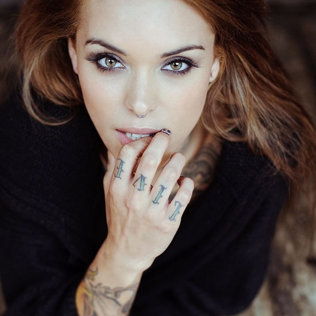 Девушка шатенка с пирсингом в носу и татуировкой на руке