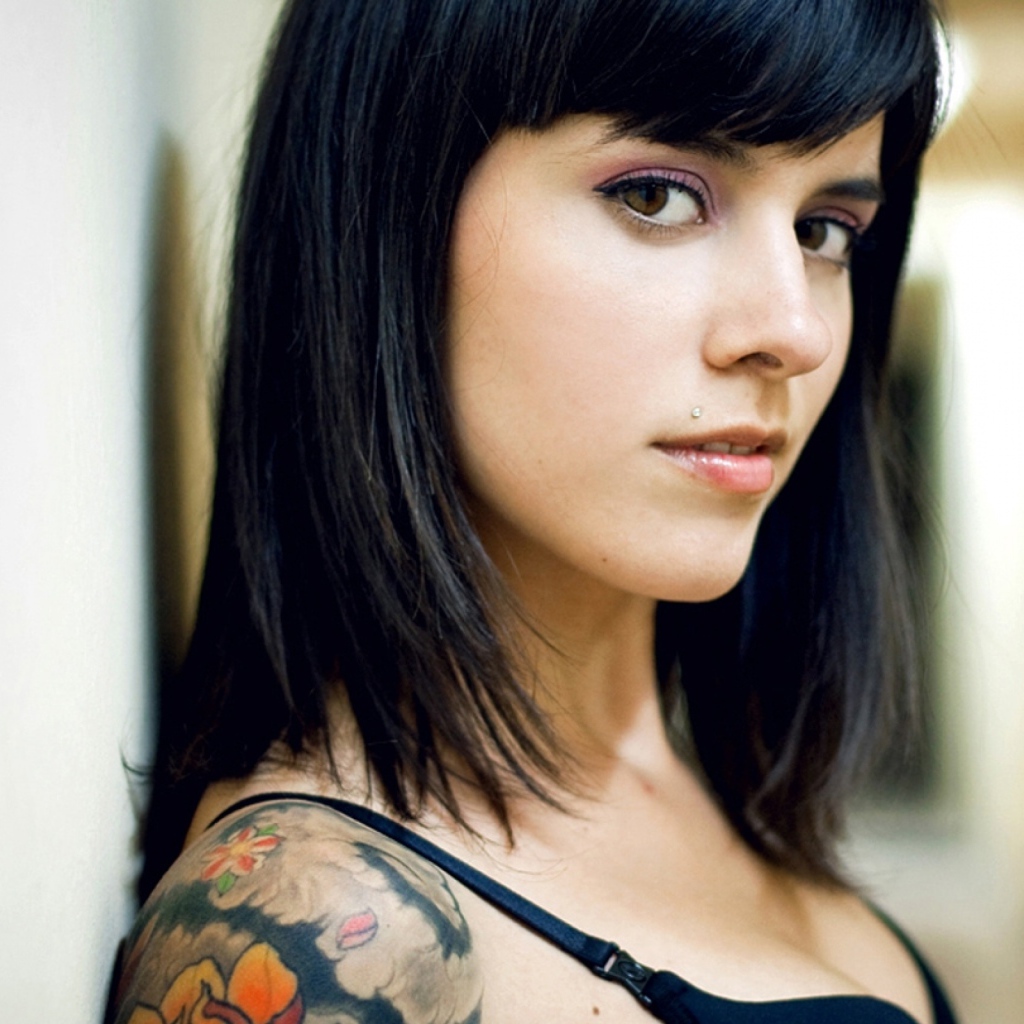 Девушка брюнетка с пирсингом в губе и татуировкой на плече
