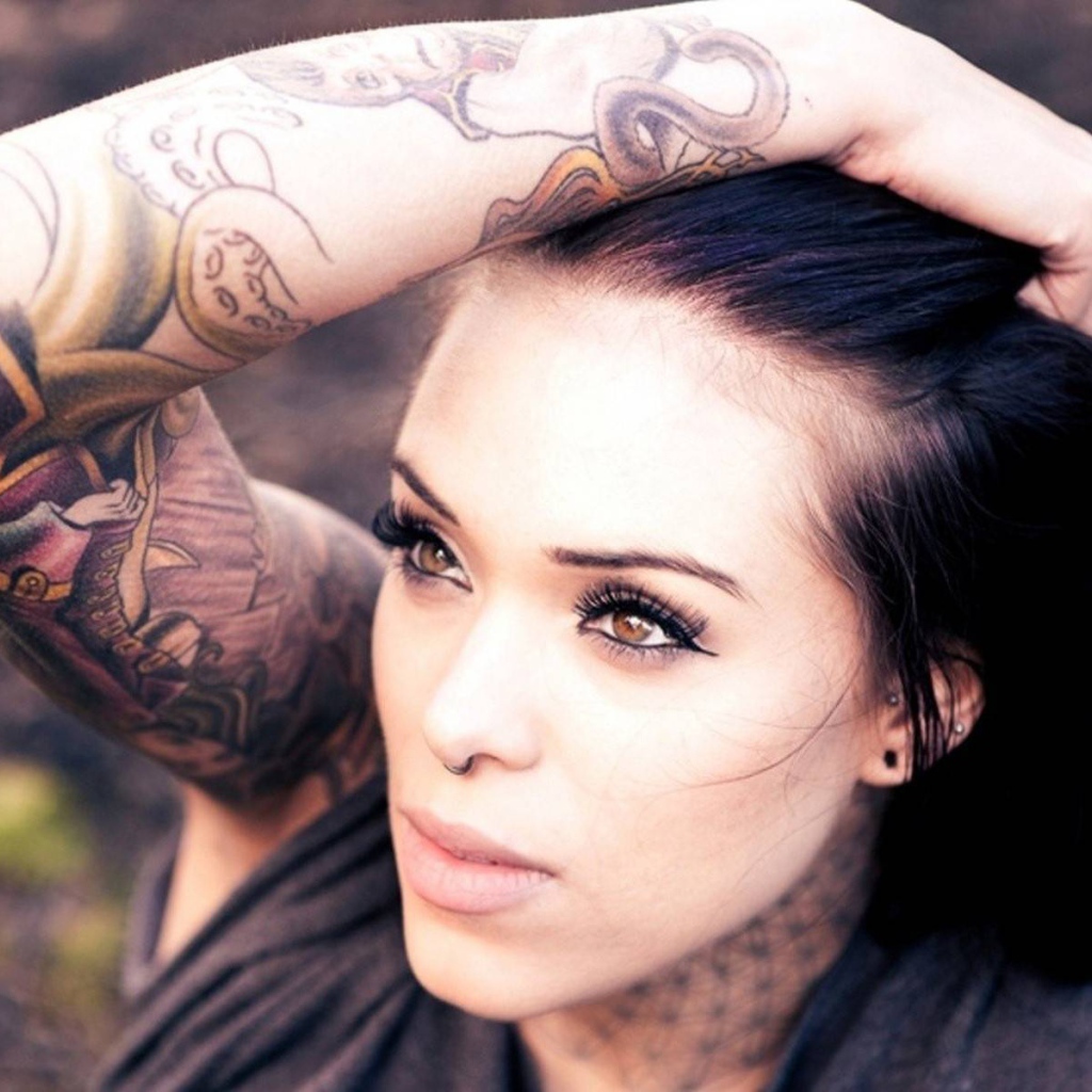 Девушка брюнетка с пирсингом в носу и татуировкой на руке